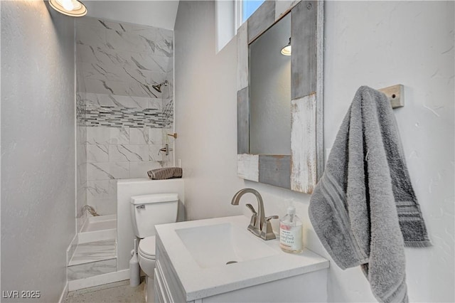 bathroom with vanity, tiled shower, and toilet