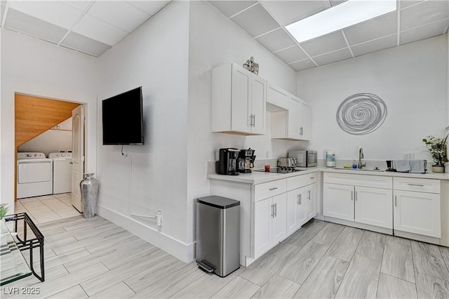 kitchen featuring white cabinetry, sink, washing machine and dryer, a drop ceiling, and black electric cooktop