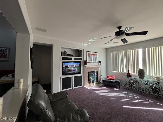 carpeted living room with ceiling fan, visible vents, built in features, and a tiled fireplace