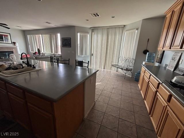 kitchen featuring dark countertops, visible vents, a glass covered fireplace, open floor plan, and a sink