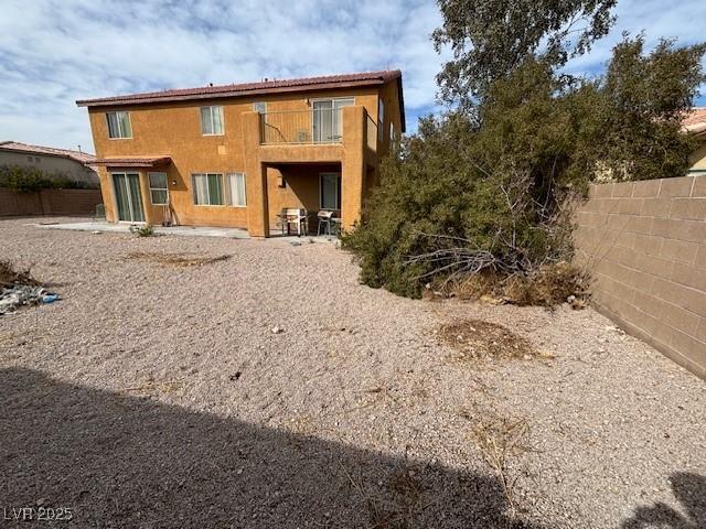 rear view of property featuring a patio area, fence, and a balcony