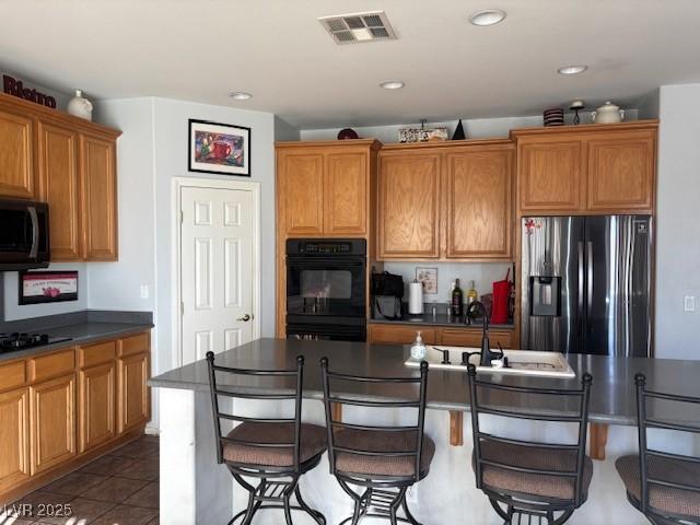 kitchen featuring a sink, visible vents, brown cabinets, black appliances, and dark countertops