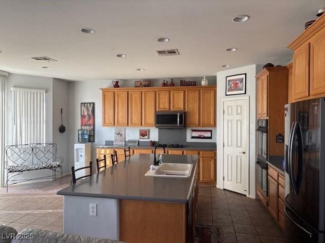 kitchen with a center island with sink, dark countertops, visible vents, a sink, and black appliances