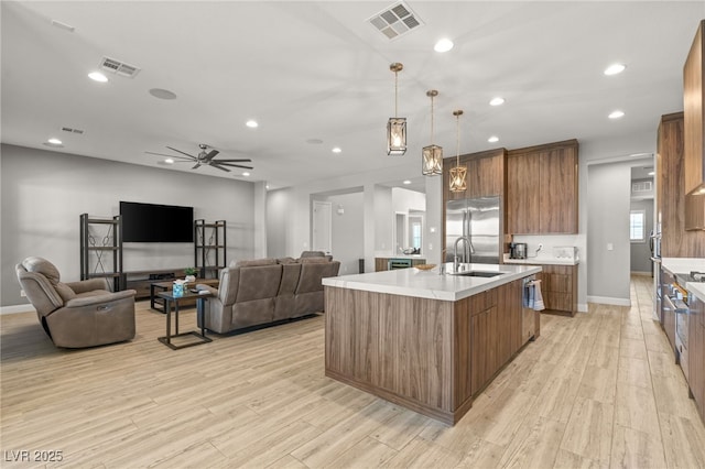 kitchen with pendant lighting, sink, light hardwood / wood-style flooring, appliances with stainless steel finishes, and an island with sink