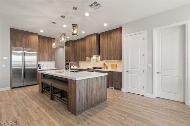 kitchen featuring pendant lighting, stainless steel built in refrigerator, an island with sink, sink, and custom exhaust hood