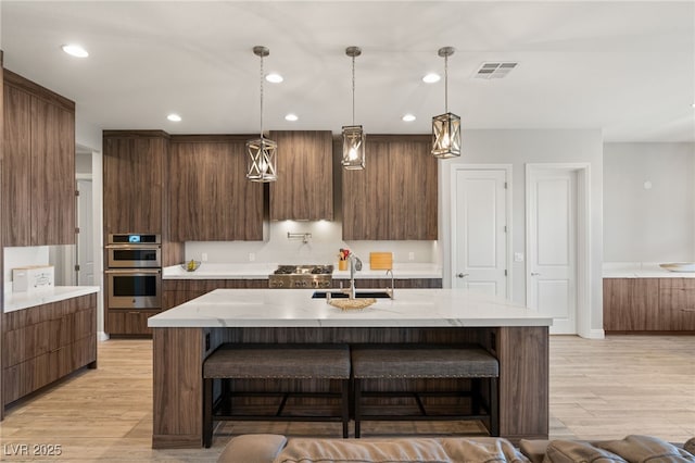 kitchen featuring a breakfast bar, sink, decorative light fixtures, light wood-type flooring, and an island with sink