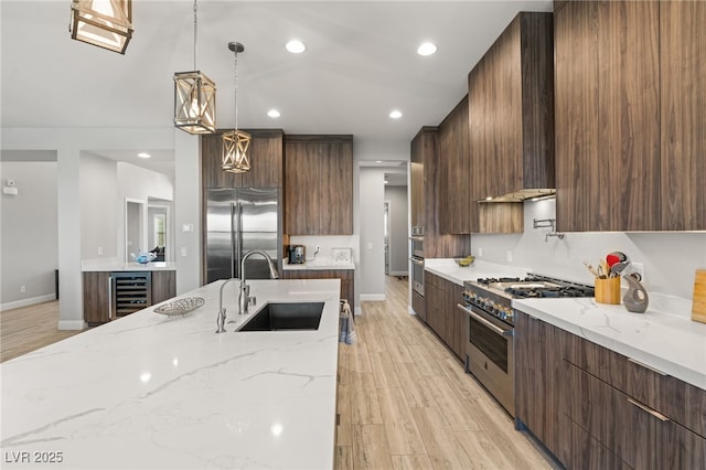 kitchen featuring sink, high end appliances, hanging light fixtures, beverage cooler, and light stone countertops