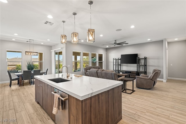 kitchen featuring pendant lighting, sink, a kitchen island with sink, light hardwood / wood-style floors, and stainless steel dishwasher