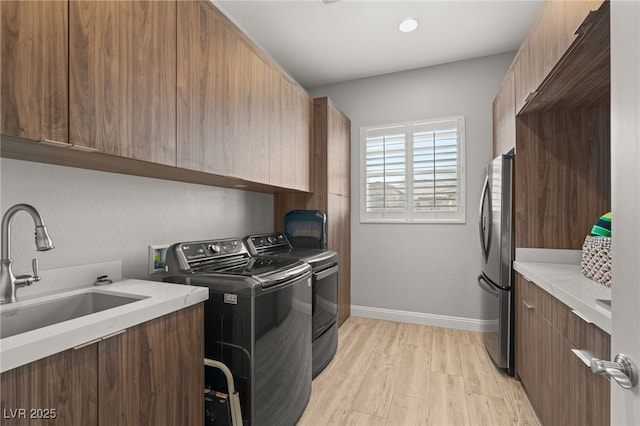 washroom with washer and dryer, sink, cabinets, and light wood-type flooring