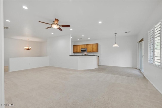 unfurnished living room with ceiling fan with notable chandelier and light carpet