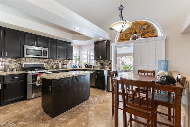 kitchen with dark cabinetry, a kitchen island, stainless steel appliances, decorative backsplash, and decorative light fixtures