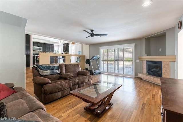 living area featuring ceiling fan, light wood-style floors, and a tile fireplace