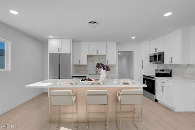 kitchen featuring white cabinetry, a kitchen bar, a center island, stainless steel appliances, and light wood-type flooring