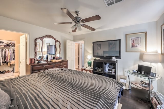 bedroom featuring a walk in closet, dark hardwood / wood-style floors, and ceiling fan