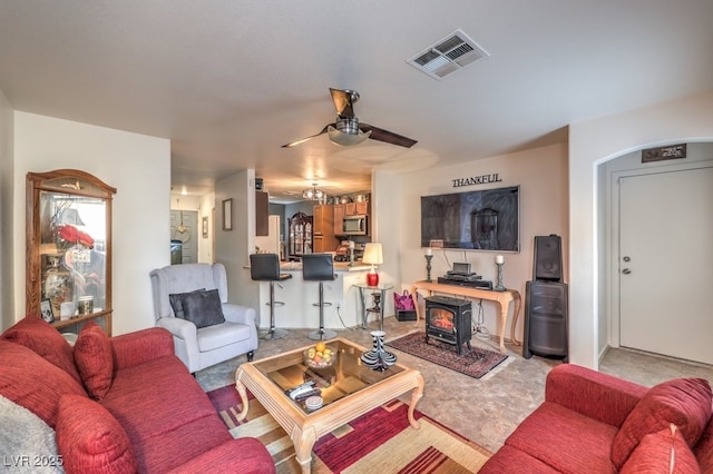 living room with a wood stove, light colored carpet, and ceiling fan