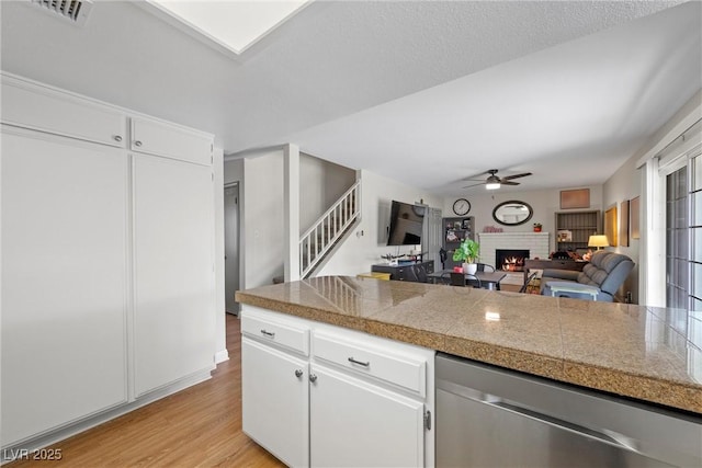 kitchen with a fireplace, white cabinets, stainless steel dishwasher, ceiling fan, and light hardwood / wood-style floors