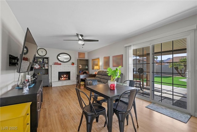 dining room with ceiling fan, a brick fireplace, and light wood-type flooring