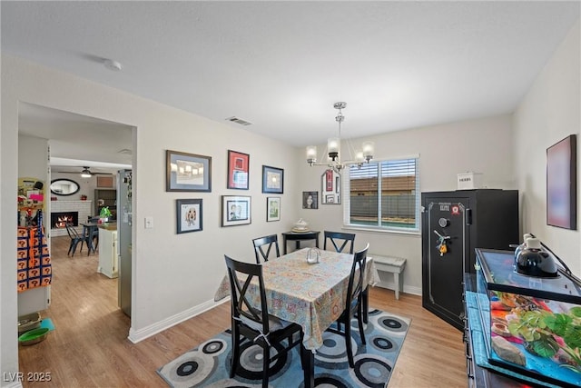 dining area with a fireplace, ceiling fan with notable chandelier, and light hardwood / wood-style flooring