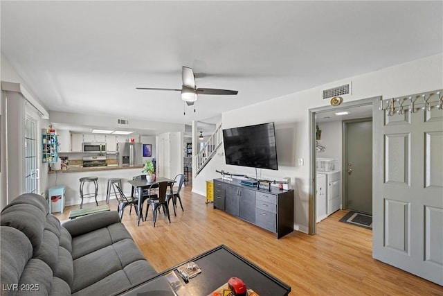 living room featuring independent washer and dryer, ceiling fan, and light wood-type flooring