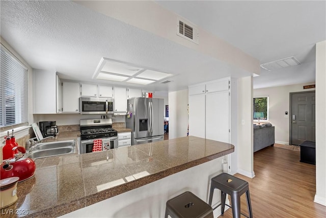 kitchen featuring dark hardwood / wood-style floors, sink, white cabinets, kitchen peninsula, and stainless steel appliances