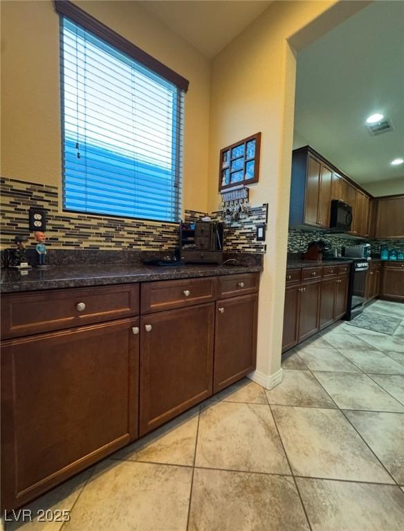 kitchen with dark stone countertops, range with electric cooktop, tasteful backsplash, dark brown cabinetry, and light tile patterned flooring