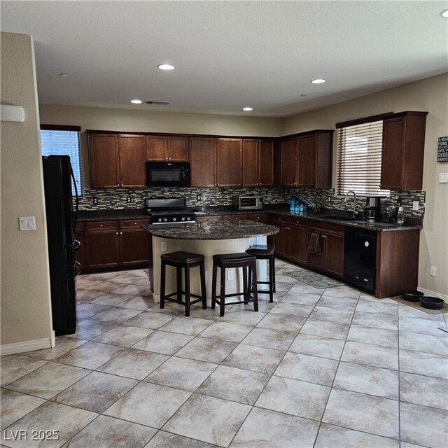 kitchen featuring sink, tasteful backsplash, a center island, a kitchen breakfast bar, and black appliances