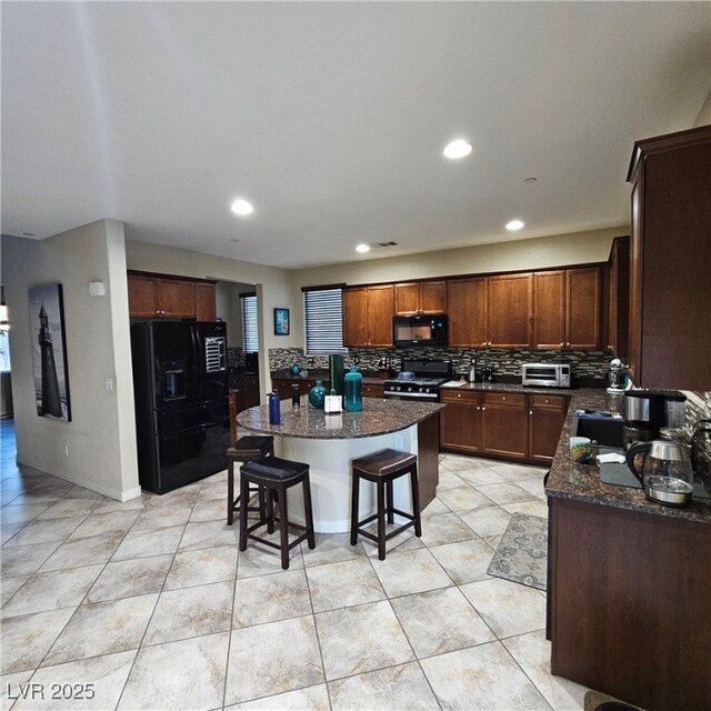 kitchen with a kitchen bar, dark stone countertops, a kitchen island, decorative backsplash, and black appliances