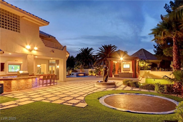 yard at dusk featuring exterior kitchen and a patio