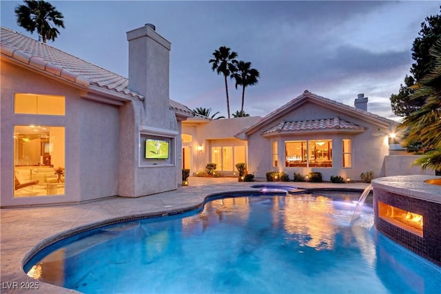 pool at dusk featuring pool water feature, an in ground hot tub, and a patio