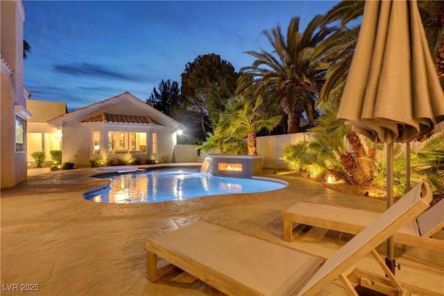 pool at dusk featuring an outbuilding, pool water feature, an in ground hot tub, and a patio