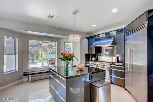 kitchen featuring backsplash, premium appliances, an island with sink, decorative light fixtures, and exhaust hood