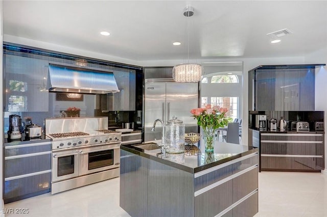 kitchen featuring pendant lighting, sink, premium range hood, stainless steel appliances, and a center island with sink