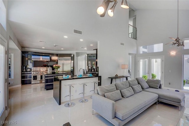 living room featuring sink, a towering ceiling, ceiling fan with notable chandelier, and french doors