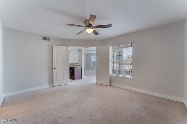 unfurnished room with light colored carpet, beverage cooler, and ceiling fan