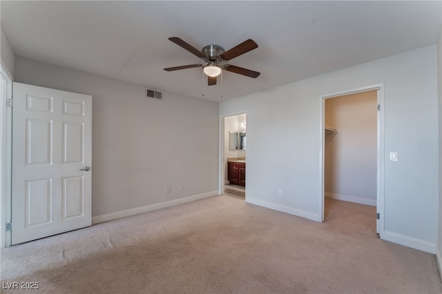 unfurnished bedroom featuring ensuite bathroom, a walk in closet, light colored carpet, ceiling fan, and a closet