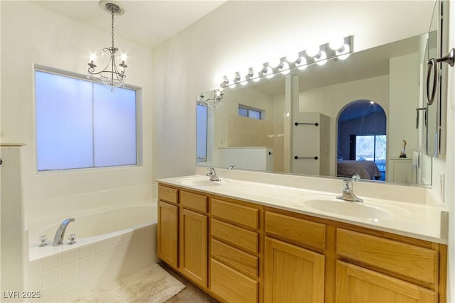 bathroom featuring vanity, tiled tub, and an inviting chandelier