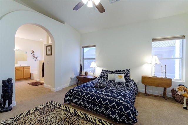 bedroom featuring ceiling fan, connected bathroom, vaulted ceiling, and light carpet