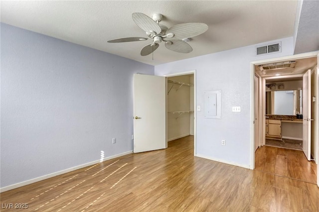 unfurnished bedroom with ceiling fan, electric panel, wood-type flooring, a spacious closet, and a closet