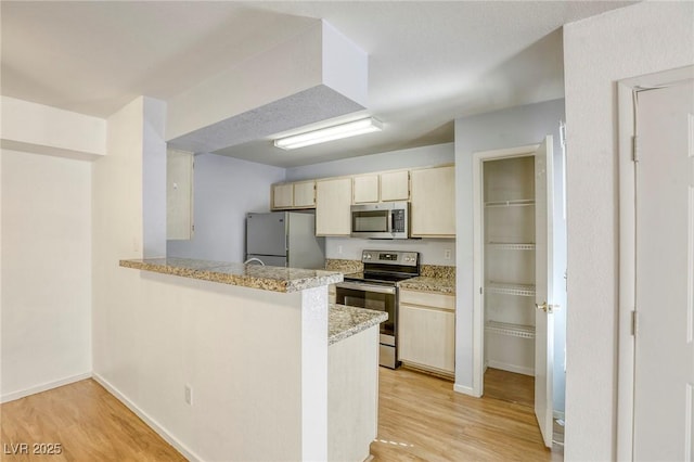 kitchen featuring light stone counters, light hardwood / wood-style flooring, kitchen peninsula, and appliances with stainless steel finishes