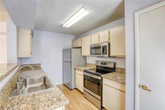 kitchen with stainless steel appliances, sink, a textured ceiling, and light wood-type flooring