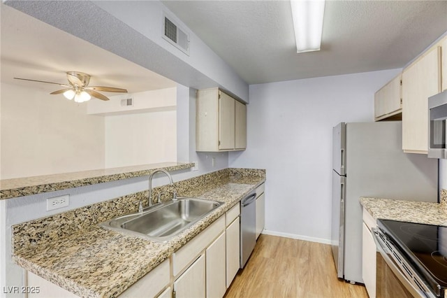 kitchen featuring sink, appliances with stainless steel finishes, light stone counters, cream cabinetry, and light wood-type flooring