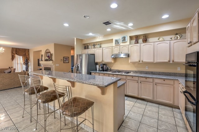 kitchen with a breakfast bar, light brown cabinets, stainless steel appliances, light stone countertops, and a center island with sink