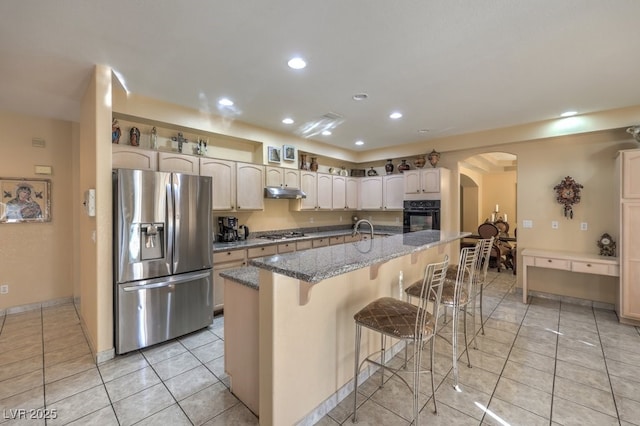 kitchen featuring light tile patterned floors, a kitchen island with sink, a kitchen bar, stainless steel appliances, and stone countertops