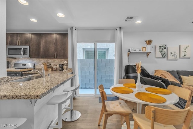 kitchen featuring sink, stainless steel appliances, dark brown cabinetry, tasteful backsplash, and light stone countertops