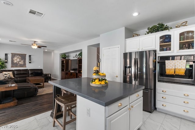 kitchen with white cabinets, a kitchen island, oven, and stainless steel fridge