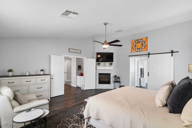 bedroom featuring vaulted ceiling, dark hardwood / wood-style floors, ceiling fan, a high end fireplace, and a barn door