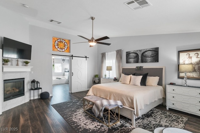 bedroom featuring lofted ceiling, a tile fireplace, dark hardwood / wood-style floors, connected bathroom, and a barn door