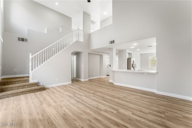 unfurnished living room with sink, light hardwood / wood-style floors, and a high ceiling