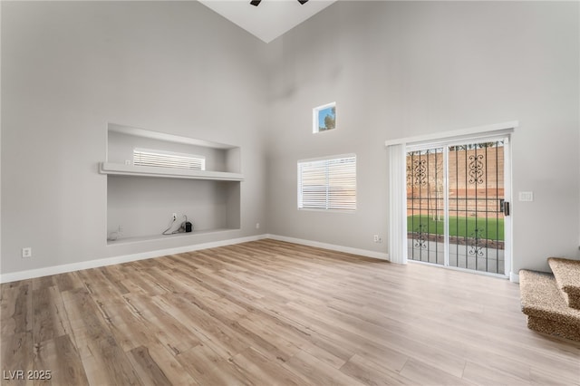 unfurnished living room featuring a high ceiling, ceiling fan, light hardwood / wood-style floors, and built in shelves