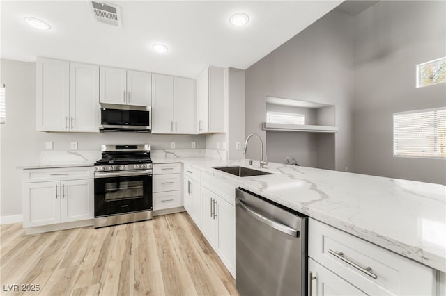 kitchen featuring sink, white cabinetry, light stone counters, light hardwood / wood-style flooring, and appliances with stainless steel finishes